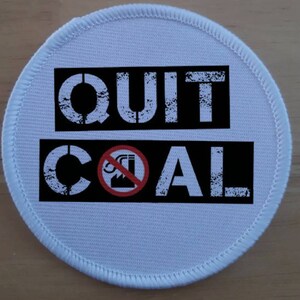 May include: White round patch with black text that reads "QUIT COAL" with a red circle and a black factory with smoke coming out of it in the middle of the word "COAL".