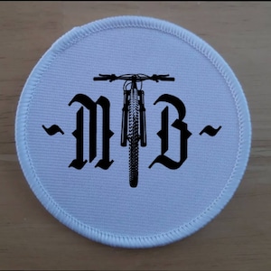 May include: White round patch with black embroidered text "MTB" and a black silhouette of a mountain bike in the center.