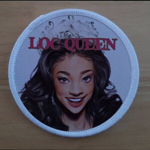 Könnte beinhalten: Ein runder weißer Patch mit weißem Rand und einem Cartoon-Bild einer Frau mit langen schwarzen Haaren, die eine Krone trägt. Der Text "LOC QUEEN" ist in rosa Buchstaben über dem Kopf der Frau geschrieben.