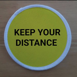 May include: A yellow round fabric patch with a white border. The patch has the text "KEEP YOUR DISTANCE" in black.