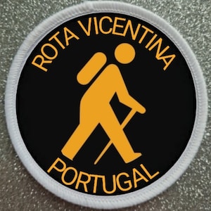 May include: A white circular patch with black and orange text and a hiker icon. The text reads "Rota Vicentina Portugal".
