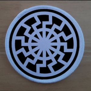 Könnte beinhalten: Ein weißer Patch mit einem schwarzen Sonnenrad-Symbol. Das Symbol ist ein Kreis mit 12 Speichen, jede mit einem Zickzackmuster.