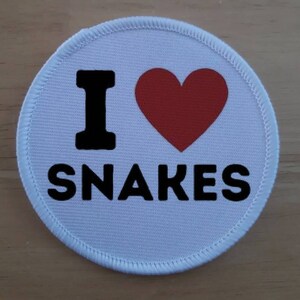 Op de afbeelding: Ronde witte patch met een rood hart en de tekst "Ik hou van slangen" in zwart.