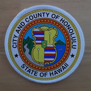 May include: White circular patch with a gold border and the text "City and County of Honolulu State of Hawaii". The center features a colorful crest with a green shield, a yellow star, and a blue and red striped banner.