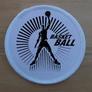 May include: White round patch with a black silhouette of a basketball player dunking a ball. The text "BASKETBALL" is printed in black letters.
