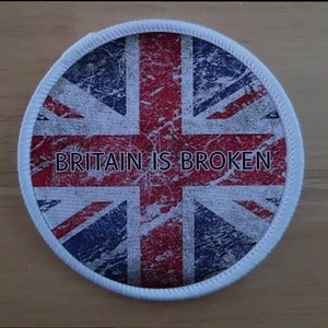 Könnte beinhalten: Runder Aufnäher mit dem Union Jack-Design im Used-Look. Der Text „BRITAIN IS BROKEN“ ist mittig platziert. Der Aufnäher hat einen weißen, genähten Rand.