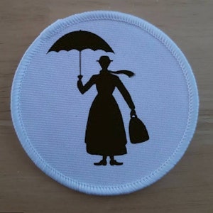 Puede incluir: Un parche redondo blanco con una silueta negra de una mujer sosteniendo un paraguas y una bolsa. La mujer lleva un sombrero y una bufanda.