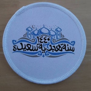 Puede incluir: Parche redondo de tela blanca con un diseño azul y gris de una mezquita y texto árabe que dice "Shahada wa Eid Mubarak 1443".