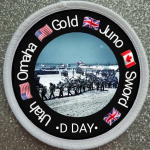 May include: A black and white circular patch with a white border. The patch features a photo of soldiers walking on a beach. The text "D DAY" is printed in white on the patch. The text "Omaha", "Utah", "Gold", "Juno", and "Sword" are printed around the photo in a circle. The flags of the United States, United Kingdom, and Canada are printed around the photo.