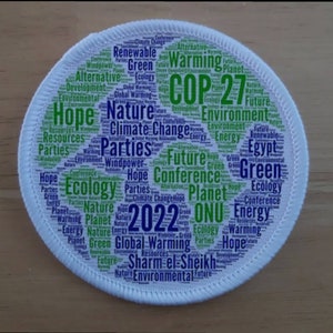 May include: A white circular patch with a green and blue word cloud. The word cloud features the text "COP 27" in large green letters. Other words in the word cloud include "nature", "climate change", "future", "green", "ecology", "planet", "energy", "hope", "parties", "resources", "environment", "global warming", "sharm el-sheikh", "2022", and "onu".