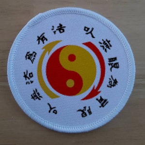May include: White round patch with a black embroidered yin yang symbol in the center. The yin yang symbol is surrounded by a circle of black text in Chinese characters.