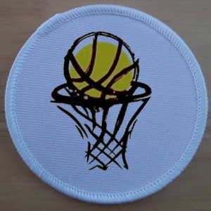 May include: A white round patch with a black and yellow basketball going through a black hoop. The basketball has a yellow centre and black lines.