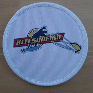 Op de afbeelding: Ronde witte patch met een rood, geel en blauw logo met de tekst "KITESURFING EXPERIENCE" en een silhouet van een persoon die kitesurft.