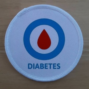 May include: White round fabric patch with a blue circle and a red blood drop in the center. The text "DIABETES" is printed below the circle.