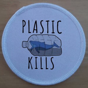 Puede incluir: Parche redondo blanco con una ballena azul atrapada dentro de una botella de plástico. El texto "PLASTIC KILLS" está impreso en negro.