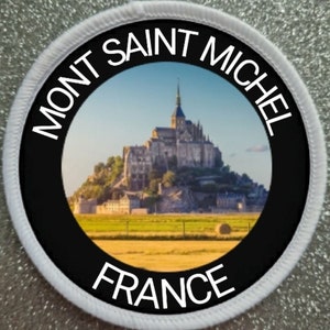 Könnte beinhalten: Ein weißer runder Patch mit schwarzem Rand und einem Bild vom Mont Saint-Michel in Frankreich. Der Text "MONT SAINT MICHEL FRANCE" ist in Weiß auf dem Patch gedruckt.