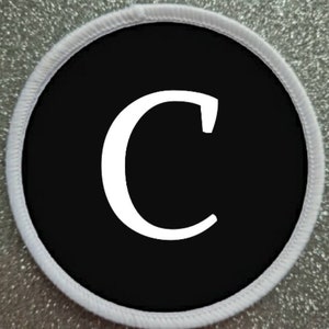 Op de afbeelding: Witte letter C op een zwarte ronde patch met een witte rand.