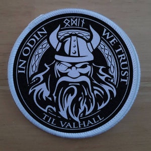 May include: A black and white circular patch with a Viking warrior wearing a horned helmet. The patch has the text "In Odin We Trust" and "Til Valhalla" around the warrior.
