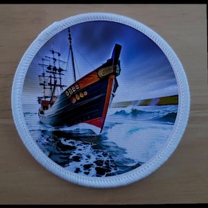 May include: A white circular patch with a blue and black ship sailing on a stormy sea. The ship has a brown and orange hull and white sails. The ship is sailing through waves with white foam.