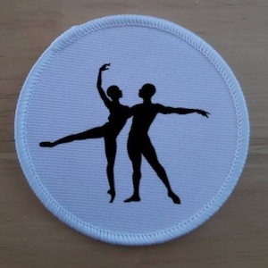 Könnte beinhalten: Runder Stoff-Patch in Weiß mit einer schwarzen Silhouette von zwei Tänzern, einer Frau und einem Mann, in einer Ballet-Pose.