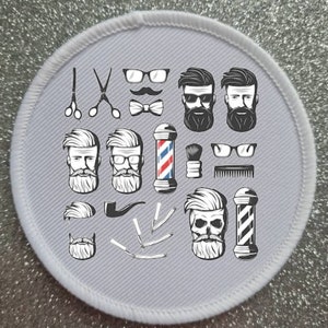 May include: A white round patch with a gray background featuring a variety of black and white illustrations related to a barbershop. The illustrations include a barber pole, scissors, razors, combs, a pipe, a mustache, glasses, and several different styles of beards.