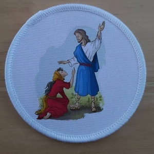 May include: A white round patch with a colourful illustration of a woman kneeling and looking up at a man with his hand raised. The man is wearing a blue robe and the woman is wearing a red dress.