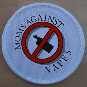 May include: White round patch with a red circle and a diagonal line through it. The circle contains a black and gray image of a vape. The text "MOMS AGAINST VAPES" is written around the circle.
