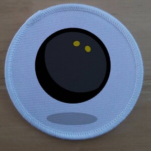 May include: White round fabric patch with a black and white image of a black ball with two yellow dots.