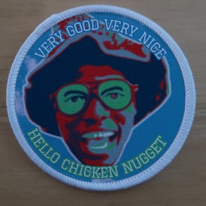 Puede incluir: Un parche redondo blanco con fondo azul y una imagen de dibujos animados de una persona con gafas de sol y un sombrero. El texto "VERY GOOD VERY NICE HELLO CHICKEN NUGGET" está escrito alrededor del borde del parche.