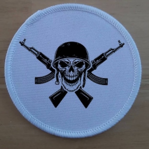 May include: White round patch with a black skull wearing a helmet and two crossed rifles.