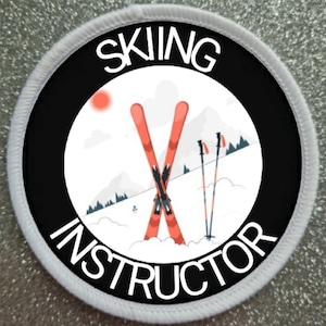 Op de afbeelding: Ronde witte patch met een zwarte rand en witte tekst die "SKIING INSTRUCTOR" luidt. Binnen de rand bevindt zich een witte cirkel met een rode zon, twee gekruiste rode ski's en twee zwarte ski-stokken.