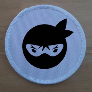 Op de afbeelding: Een ronde witte stoffen patch met een zwart silhouet van een ninja met een masker.