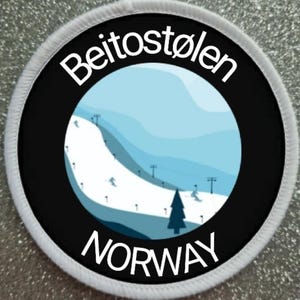 May include: A white round patch with a black border and white text. The text reads "Beitostølen NORWAY". Inside the border is a black and white illustration of a ski slope with a blue sky and mountains in the background.