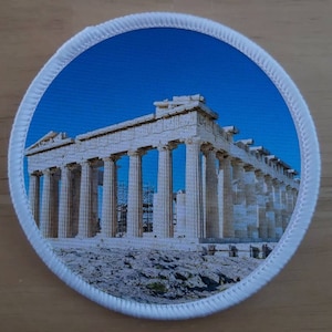 May include: A white marble structure with columns, known as the Parthenon, against a bright blue sky. The structure is located on a hill with rocky terrain.