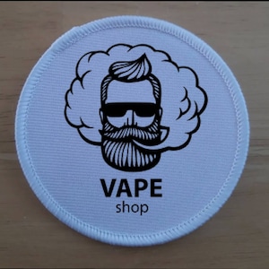 May include: White round patch with a black and white illustration of a man with a beard and sunglasses exhaling a large cloud of smoke. The text "VAPE shop" is printed below the illustration.