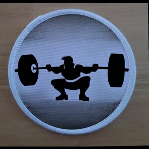 May include: A white circular patch with a black silhouette of a person performing a barbell squat.