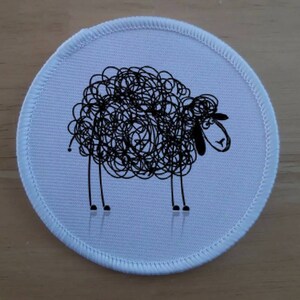 May include: White round patch with a black and white illustration of a sheep with a curly fleece.