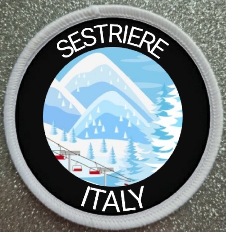 Peut inclure: Un patch circulaire blanc et noir avec une bordure blanche. Le centre du patch est noir avec un cercle blanc &agrave; l'int&eacute;rieur. Le cercle blanc pr&eacute;sente une illustration de montagne enneig&eacute;e avec un t&eacute;l&eacute;si&egrave;ge. Le texte "SESTRIERE ITALY" est imprim&eacute; en blanc sur fond noir.