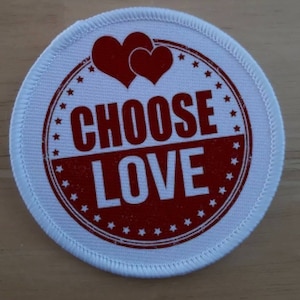 May include: White round fabric patch with red stitching around the edge. The patch has a red circle with white stars around the edge and the words "CHOOSE LOVE" in white letters.