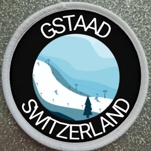 Peut inclure: Patch rond blanc avec une bordure noire et du texte blanc. Le texte dit "GSTAAD SWITZERLAND". À l'intérieur du cercle se trouve une illustration bleue et blanche d'une piste de ski avec un téléski.