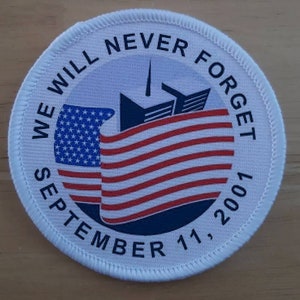 以下が含まれることがあります： 青い星と赤いストライプのアメリカ国旗、ツインタワーのシルエット、そして「We Will Never Forget September 11, 2001」というテキストが書かれた白い丸いパッチ。