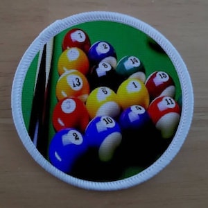 Puede incluir: Primer plano de una mesa de billar de fieltro verde con un juego de 15 bolas de billar dispuestas en forma de triángulo. Las bolas están numeradas del 1 al 15 y son de varios colores, incluidos rojo, amarillo, azul y verde.