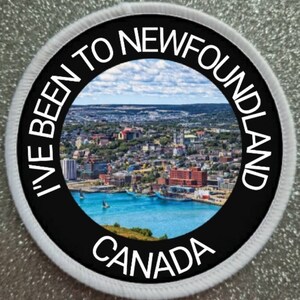 May include: A white round patch with a black circle in the centre. The black circle has white text that reads "I've Been To Newfoundland Canada" and a photo of a city skyline with a body of water in the foreground.