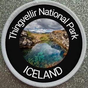 Può includere: Un cerotto rotondo bianco e nero con il testo "Thingvellir National Park Iceland" in lettere bianche. Il centro del cerotto presenta una foto di un specchio d'acqua con una costa rocciosa e un cielo nuvoloso.