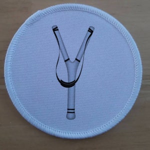 May include: White round fabric patch with a black and white slingshot design.