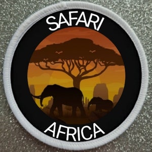 Puede incluir: Un parche circular blanco con texto negro que dice "SAFARI AFRICA" y una silueta negra y naranja de un árbol de acacia con dos elefantes caminando debajo.
