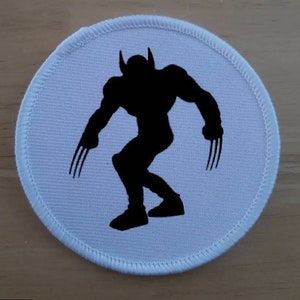 May include: A white round patch with a black silhouette of a superhero with claws.