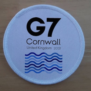 May include: White round patch with black text that reads "G7 Cornwall United Kingdom 2021". A blue and white wave design is at the bottom of the patch.