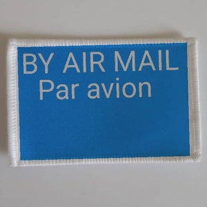 May include: A blue rectangular label with white text that reads "BY AIR MAIL Par avion".