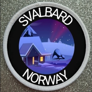 Peut inclure: Un écusson rond avec l'inscription "SVALBARD NORWAY" en blanc. L'écusson présente une scène hivernale avec une maison, de la neige et un ciel coloré. Il a une bordure noire et un bord cousu blanc.